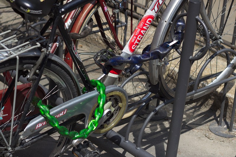 Un exemple illustrant la façon d'attacher correctement un vélo : une chaîne lie la roue avant et le cadre à un point fixe, tandis qu'une deuxième chaîne lie la roue arrière au cadre.